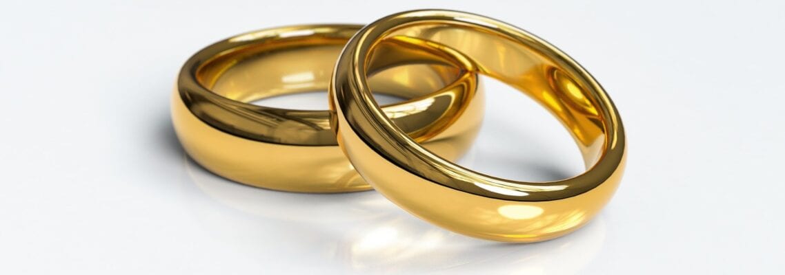 Two gold wedding rings sitting on top of a white surface.