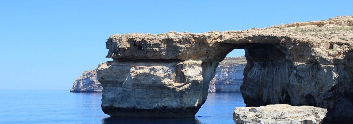 A rock formation near the ocean with water in it.