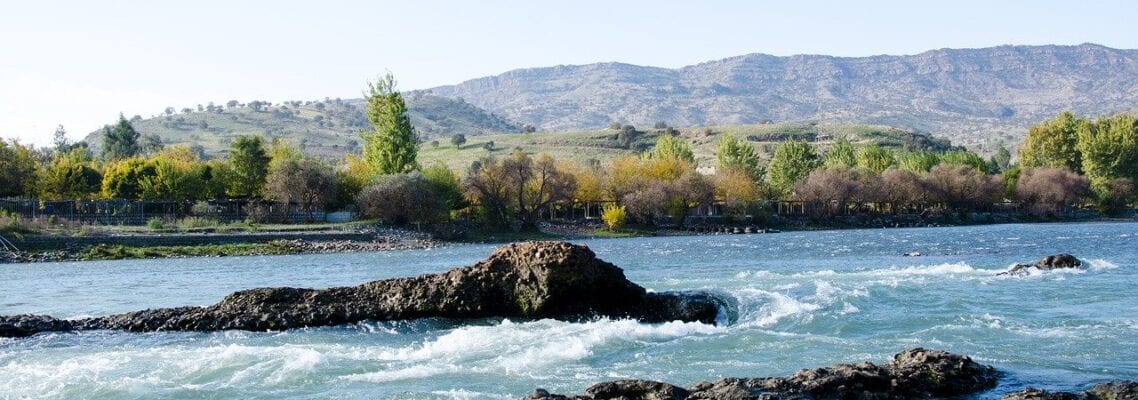 A river with rocks in the water and mountains in the background.