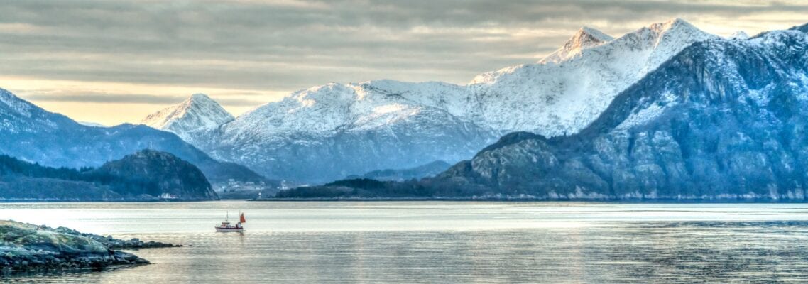 A person in a boat on the water with mountains behind them.