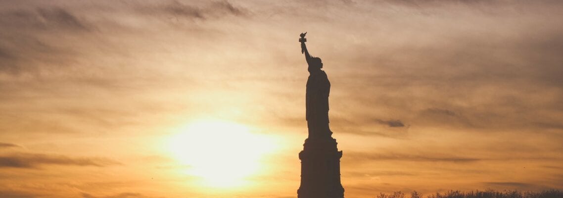 A statue of liberty is seen in the sunset.