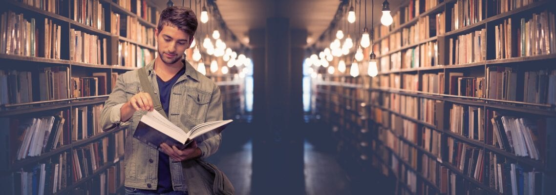 A man standing in a library holding an open book.