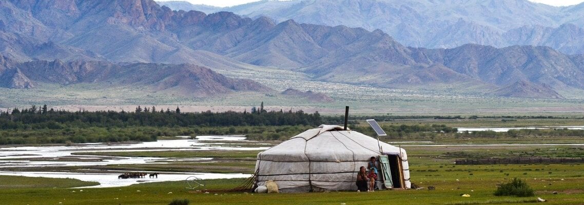 A white yurt in the middle of an open field.