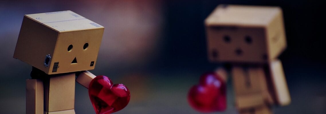 Two wooden toy figures holding a heart in each other.