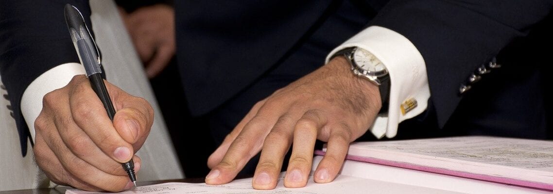 A man signing papers at a table with another person.