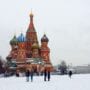 A group of people standing in the snow near a building.